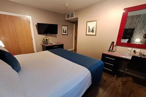 Een hotelkamer met een bed, bureau, televisie en spiegel.