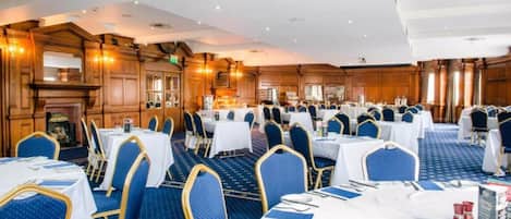 A banquet hall with multiple round tables, blue upholstered chairs, and a classic wooden interior.
