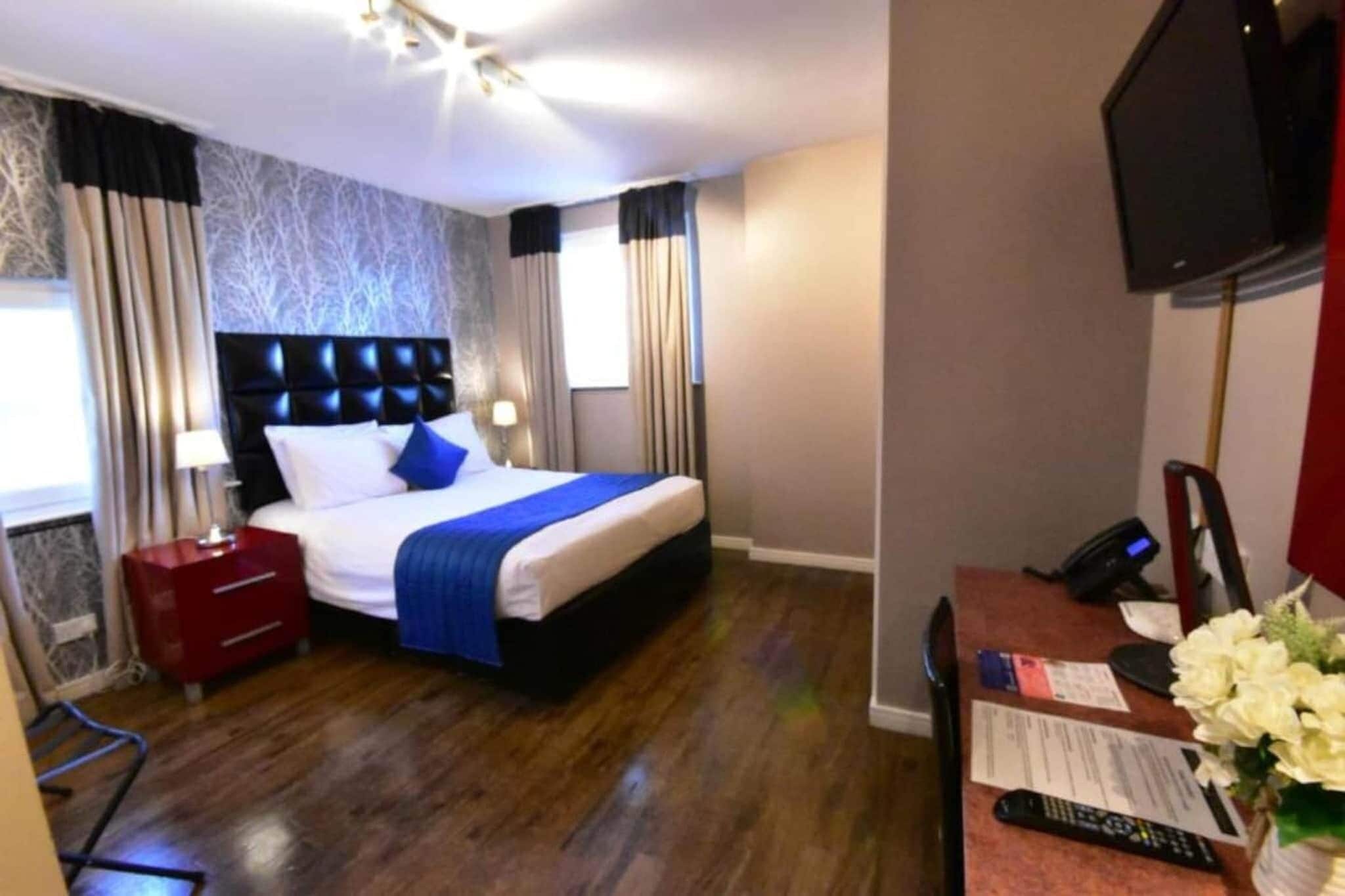 A hotel room with a bed, a desk with a telephone, a television, and a window with curtains.