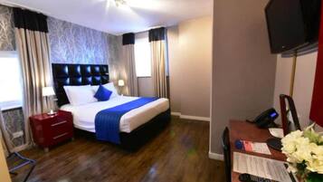 A hotel room with a bed, a desk with a telephone, a television, and a window with curtains.