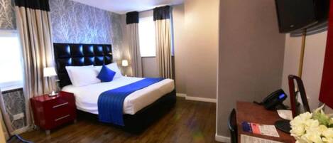 A hotel room with a bed, a desk with a telephone, a television, and a window with curtains.