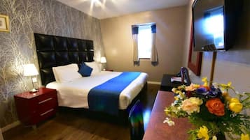 A hotel room with a bed, bedside tables, a TV, and a floral arrangement.