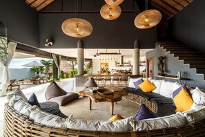 A spacious lounge area with a round seating arrangement, a central coffee table, and a staircase leading to an upper level. - Villa Magena (Badung)