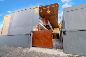 Um edifício moderno com portão de madeira, varanda e escadaria que leva a um andar superior.