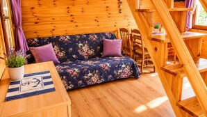 A wooden cabin interior with a sofa, a table with a placemat, a potted plant, and a staircase. - Cottages for 5 People With a Swimming Pool (Kamien Pomorski)