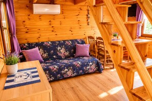 Ein Holzblockhaus-Interieur mit einer Couch, einem Tisch mit Unterlage, einer Topfpflanze und einer Treppe.