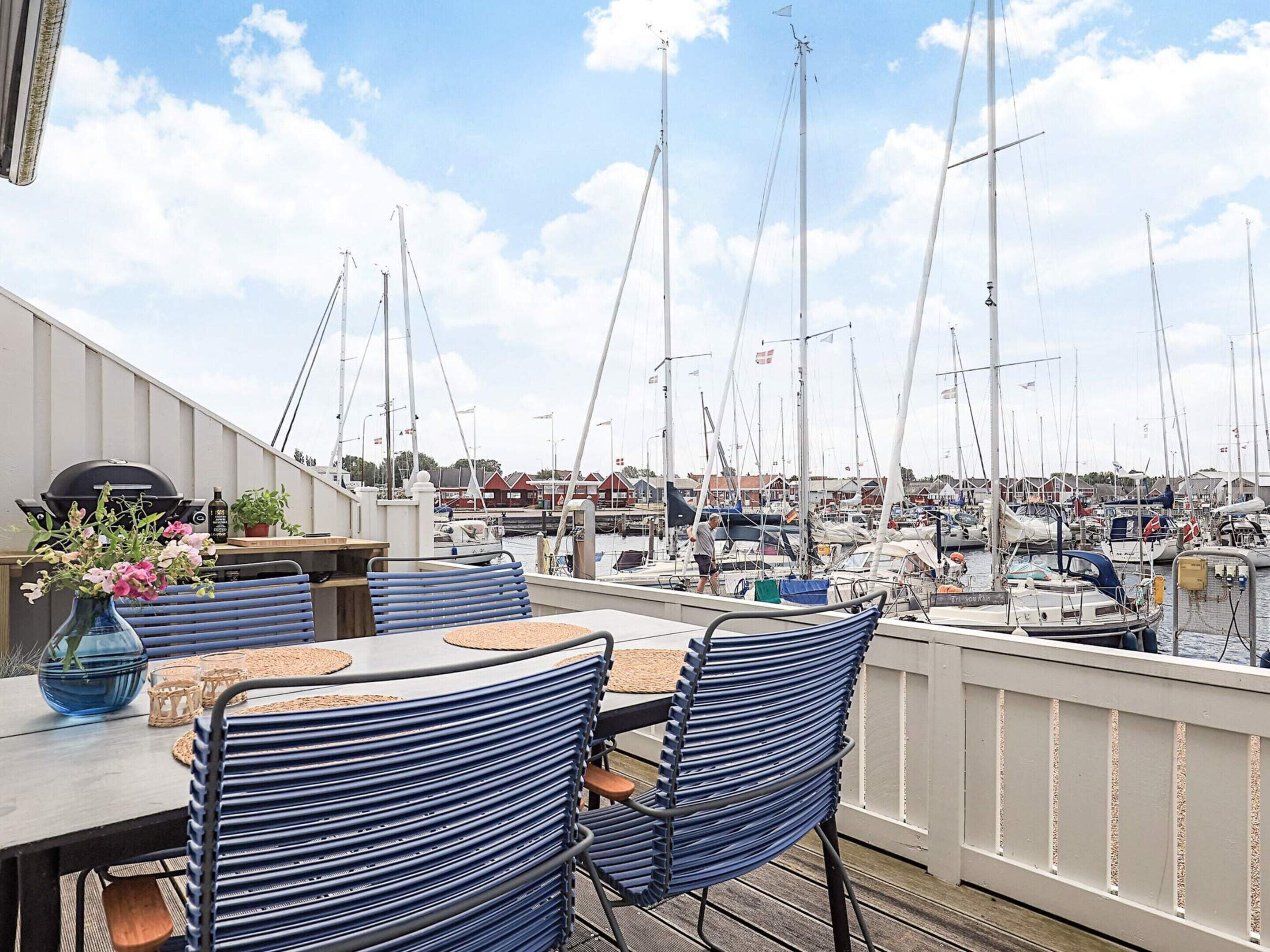 Una terraza con mesa y sillas que da a un puerto deportivo con varios veleros.