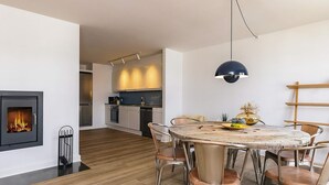 A modern kitchen with a built-in stove, a dining area with a round table and metal chairs, and a hanging pendant light.