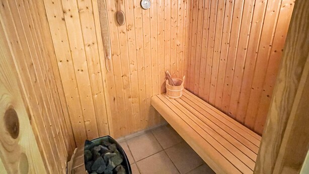 A wooden sauna with a bench, a bucket, and a container of stones.