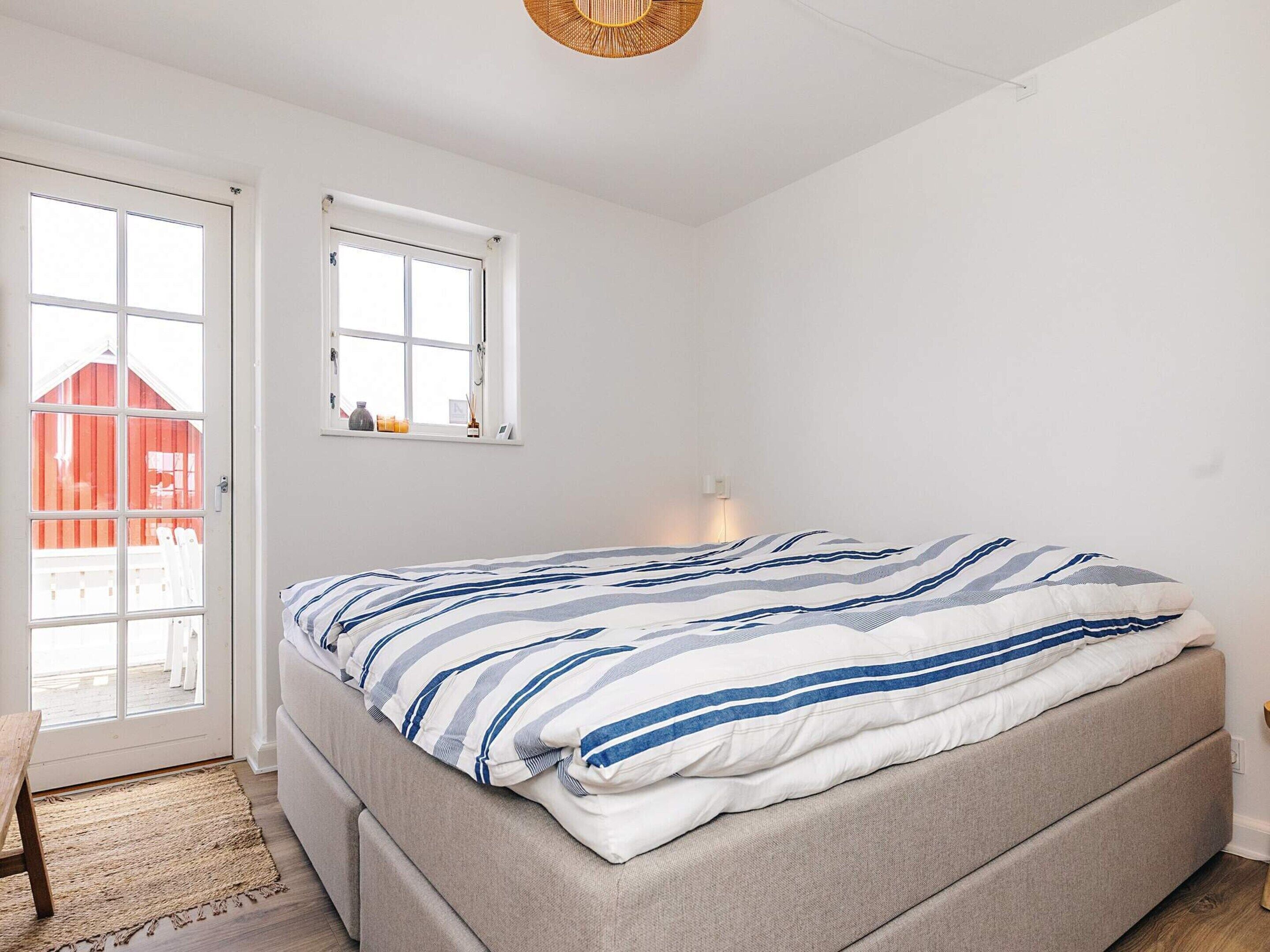 Un dormitorio con cama, ventana, puerta y vista a un edificio rojo en el exterior.