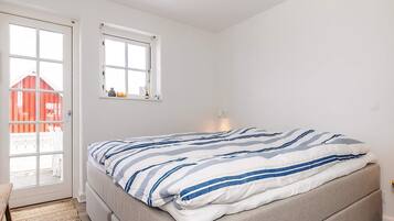 Un dormitorio con cama, ventana, puerta y vista a un edificio rojo en el exterior.