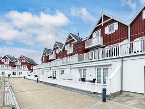 A row of red and white buildings with balconies, a gravel courtyard, and a clear sky. - 4 Star Holiday Home in Bagenkop (Sydlangeland)