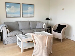 A living room with a striped sofa, a wicker chair, a white coffee table, and two framed pictures on the wall. - 4 Star Holiday Home in Bagenkop (Sydlangeland)