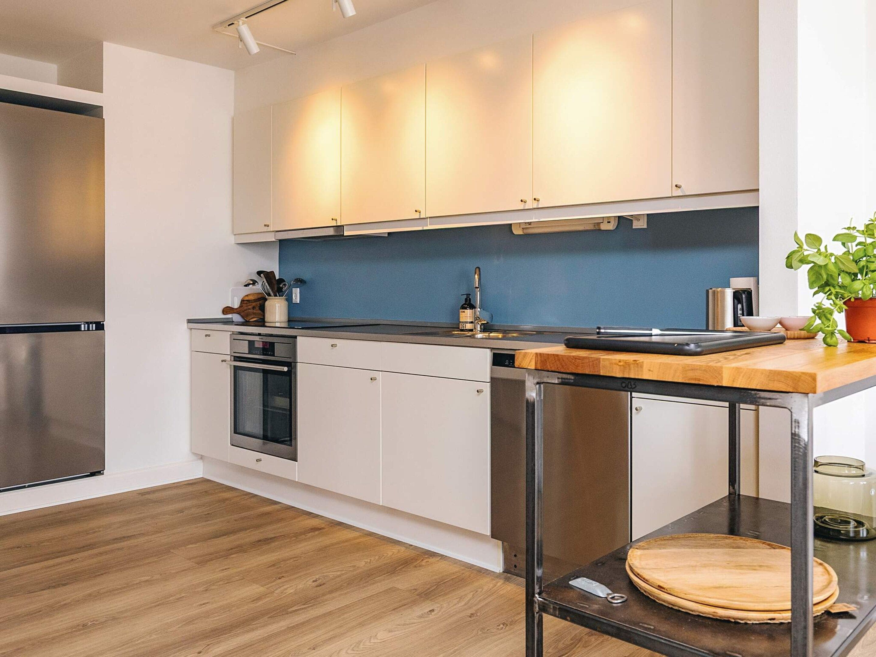 Une cuisine moderne avec des meubles blancs, des appareils en acier inoxydable, un plan de travail en bois et une plante en pot.