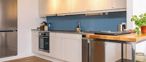 Une cuisine moderne avec des meubles blancs, des appareils en acier inoxydable, un plan de travail en bois et une plante en pot.