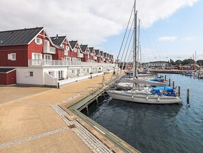 A waterfront property with a row of red and white buildings, a dock with boats, and a clear sky. - 5 Star Holiday Home in Bagenkop (Sydlangeland)