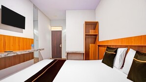 A hotel room with a bed, a TV mounted on the wall, a wooden headboard, a wooden wardrobe, and a small table with a bottle. - Bwalk Hotel Cozy Double (Malang)