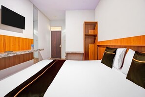 Une chambre d’hôtel avec un lit, un téléviseur fixé au mur, une tête de lit en bois, une armoire en bois et une petite table avec une bouteille.