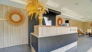 A reception desk with a modern design, a large sun decoration on the wall, and a reception area with a seating arrangement. - Bwalk Hotel Cozy Double (Malang)