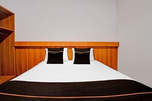 Un letto con testiera in legno, due cuscini neri e una coperta bianca.
