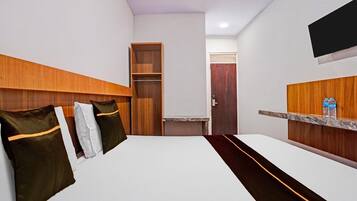 Quarto de hotel com cama, cabeceira de madeira, pequena escrivaninha, espelho e televisão fixada na parede.