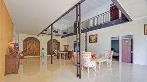 A spacious living area with a high ceiling, a staircase, and a dining area with chairs and a table. - Bwalk Hotel Cozy Double (Malang)