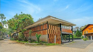 A modern building with a covered walkway, surrounded by trees and a paved area. - Bwalk Hotel Cozy Double (Malang)