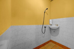 Une salle de bain avec un mur jaune, un lavabo blanc et une douche avec un flexible.