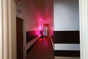 Un pasillo con una puerta al final, una planta en maceta y un marco de puerta iluminado en rojo.