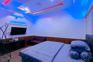 A bedroom with a bed, a TV, a desk, and a chair.