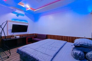 A hotel room with a bed, a TV mounted on the wall, a desk, and a chair.