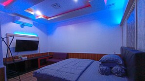 Un dormitorio con una cama, un televisor montado en la pared y un escritorio con una silla.