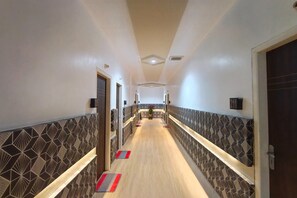En hotellkorridor med väggar som har ett mönster, ett trägolv och en central ljuskrona.