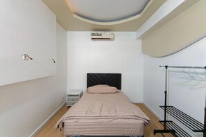 A bedroom with a bed, an air conditioning unit, a wall-mounted heater, a nightstand, and a drying rack.