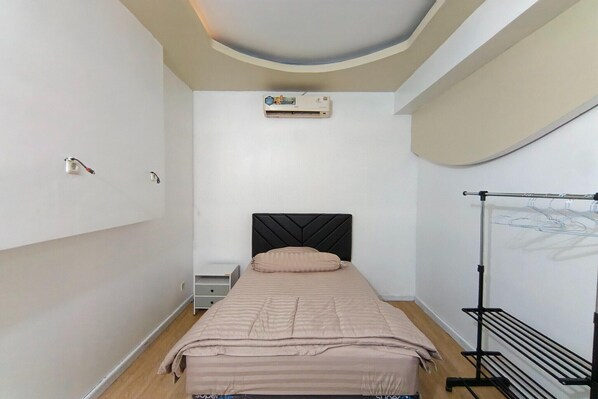 Une chambre comprenant un lit, un appareil de climatisation, un radiateur mural, une table de chevet et un étendoir.