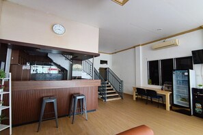 A modern interior with a wooden counter, bar stools, a staircase, a dining area, and a refrigerator.