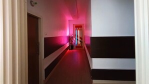 Um corredor com uma porta no fim, um vaso de planta e um batente de porta iluminado em vermelho.
