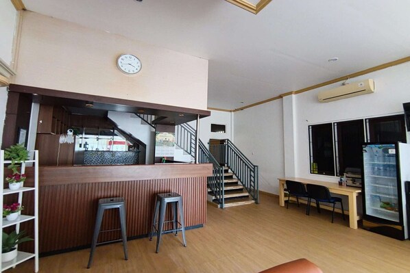 A restaurant with a wooden counter, stools, a staircase, a clock, and a refrigerator. - Esun Bue Cozy Single Stay (Palangkaraya)