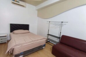 A bedroom with a bed, a red couch, a drying rack, and a small table.