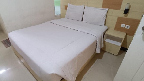 Una habitación de hotel con cama, mesita de noche y una lámpara de pared.