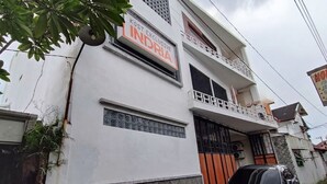 Un edificio de dos pisos con un letrero que dice 'KOST EXCLUSIVE INDIA' y un coche negro estacionado al frente.
