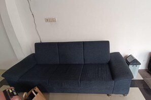 A dark-colored sofa in a room with a tiled floor and a light-colored wall.