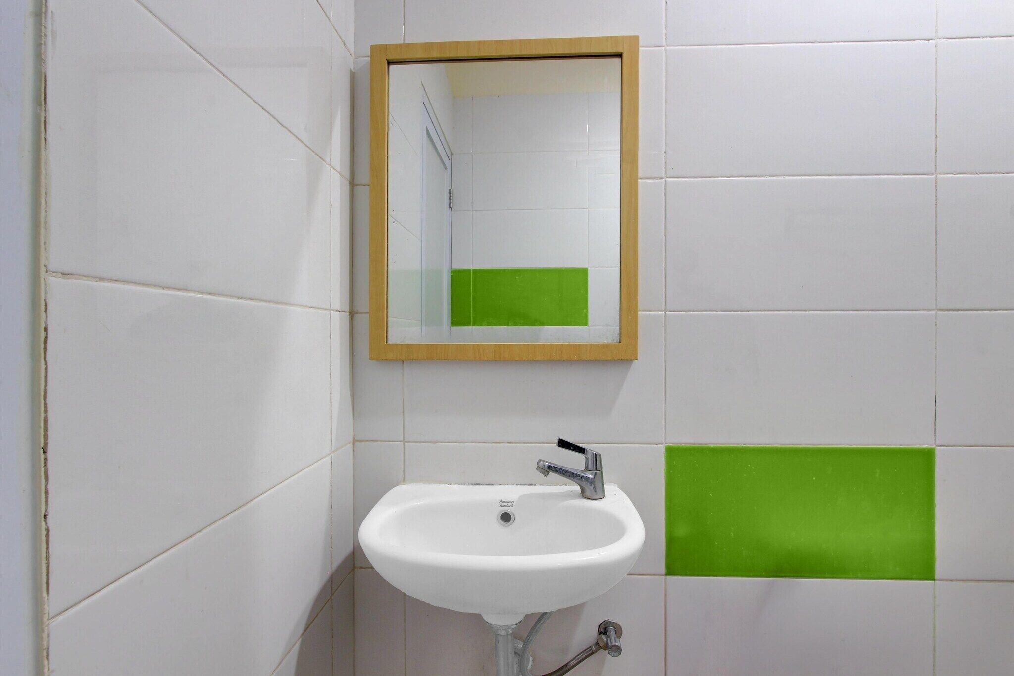 A bathroom with a white sink, a mirror, and green tiles on the wall.