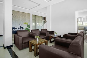 Eine moderne Hotelhalle mit braunen Ledersofas, Holztischen und einem großen Fenster mit einem Waldgemälde.