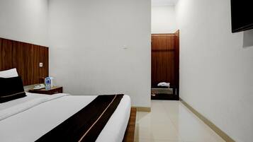 A hotel room with a bed, a bedside table with a bottle, a TV mounted on the wall, and a wooden wardrobe.