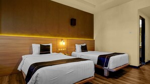 Ein Hotelzimmer mit zwei Betten, einem Holzkopfteil, einer Wandleuchte und einer Tür rechts.