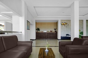 Un hall d’hôtel avec un comptoir d’accueil, deux canapés marron, une table basse en bois et un tableau représentant des oiseaux accroché au mur.