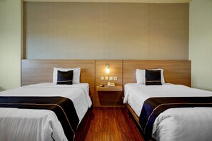 Une chambre d’hôtel avec deux lits, une tête de lit en bois, une table de chevet avec un téléphone et un luminaire fixé au mur.