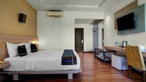 A hotel room with a bed, bedside table, TV, desk, chair, and a small refrigerator.