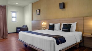 A hotel room with a large bed, a desk, a chair, a window with curtains, and a wall-mounted light.